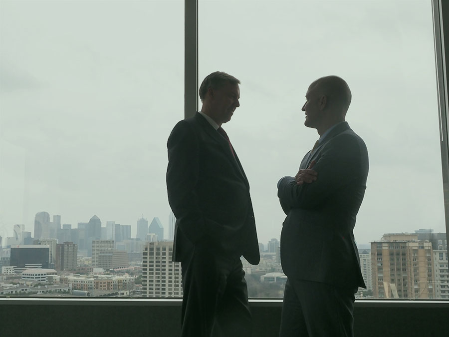 two dallas texas businessmen talking to each other in front of skyscraper window silhouette forms turtle creek dallas investment company 